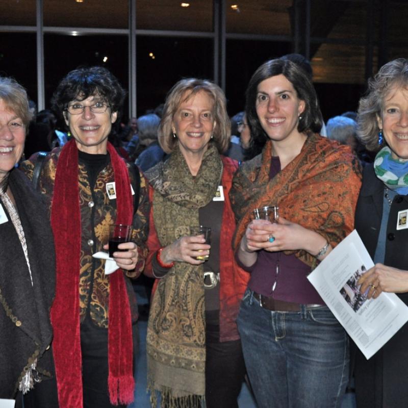 Five women stand indoors smiling.