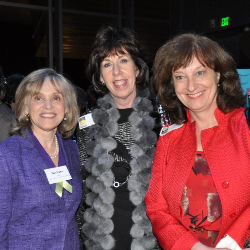 Three women stand indoors smiling.