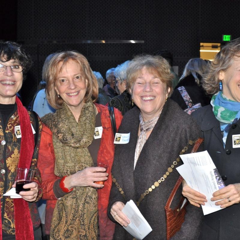 Four women stand indoors smiling.