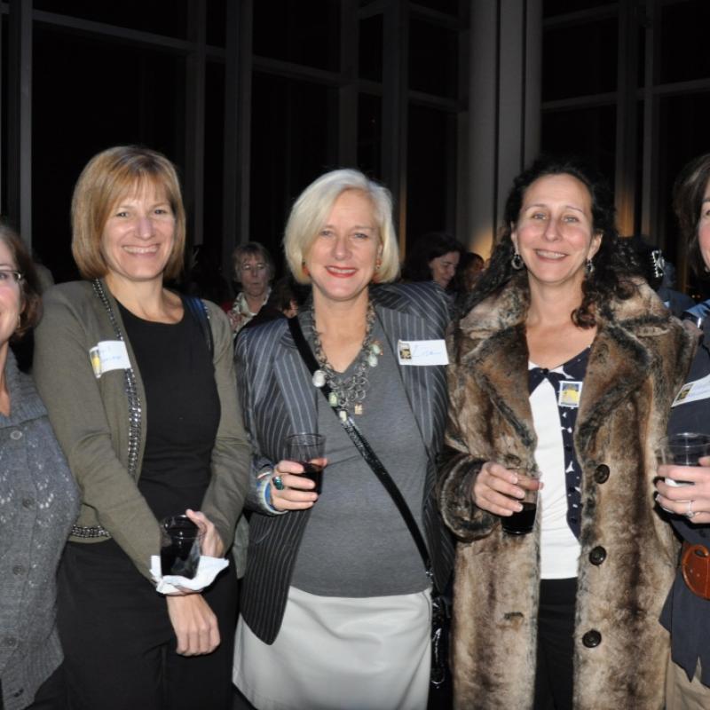 Five women stand indoors smiling.