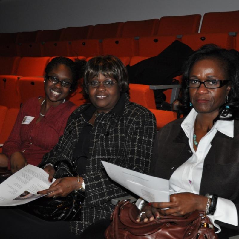 Three women sit indoors smiling.