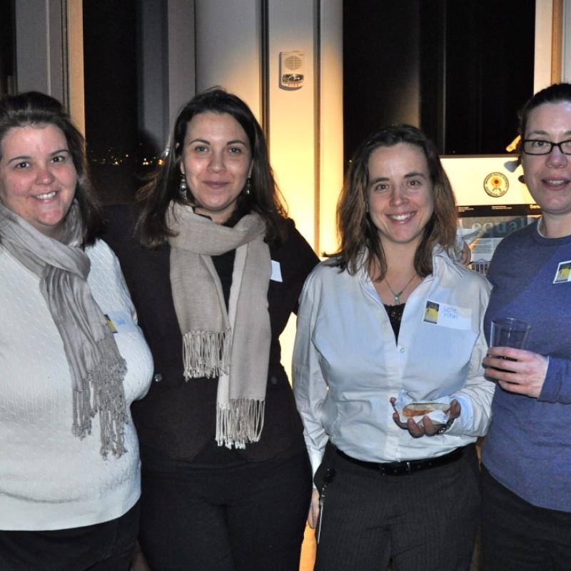 Four women stand indoors smiling.