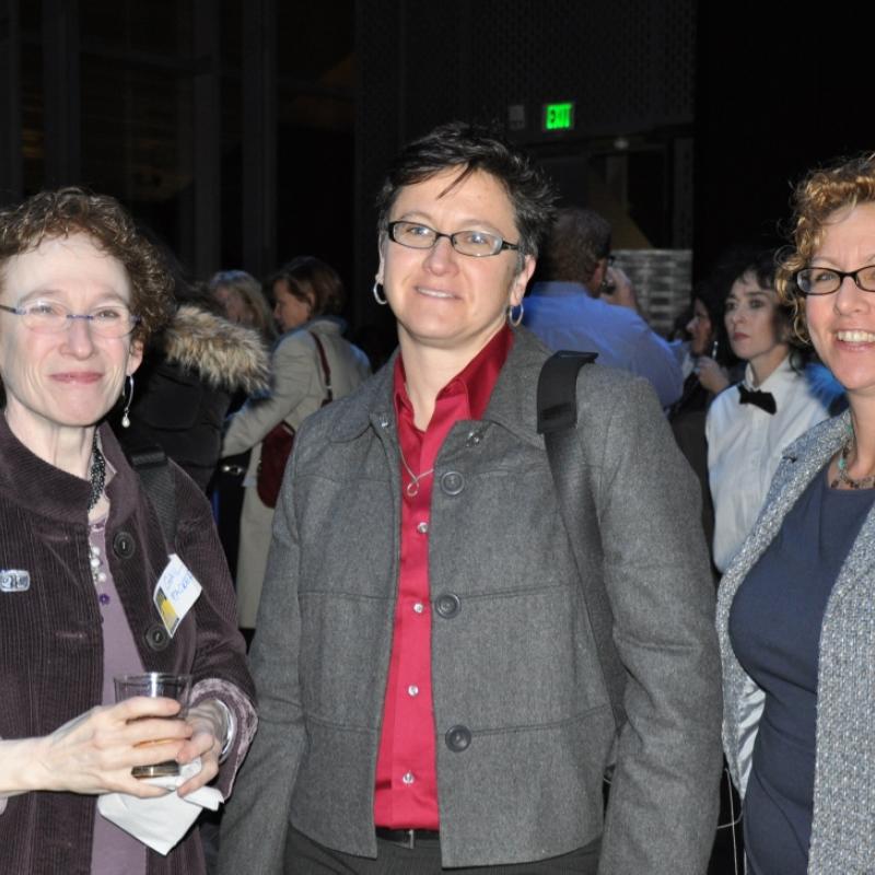 Three women stand indoors smiling.