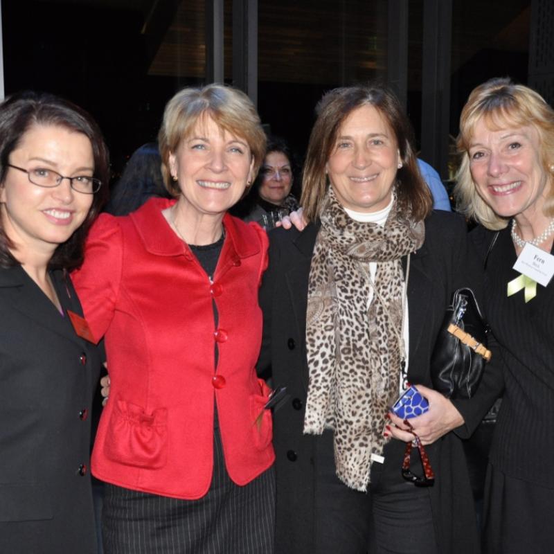 Four women stand indoors smiling.