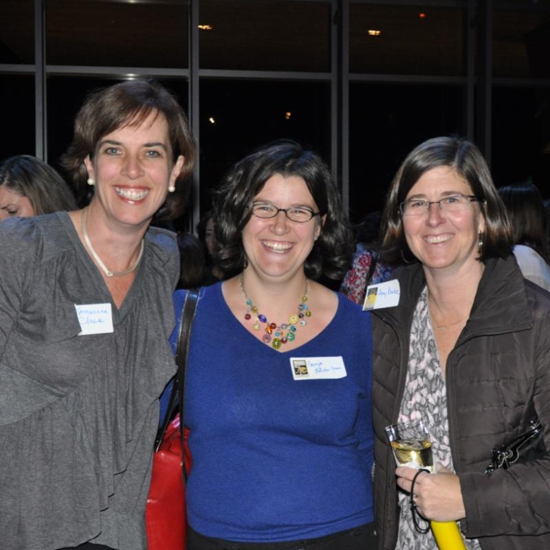 Three women stand indoors smiling.