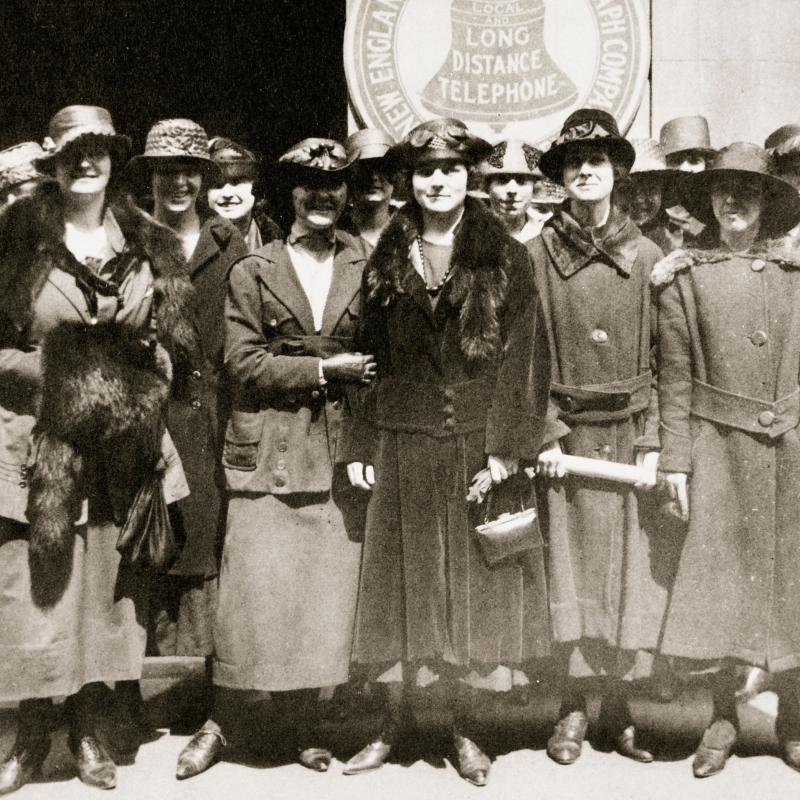 A group of elegantly dressed women, wearing hats and coats, standing outside together.