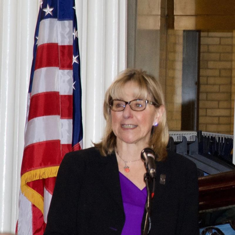 Woman stands at podium speaking.