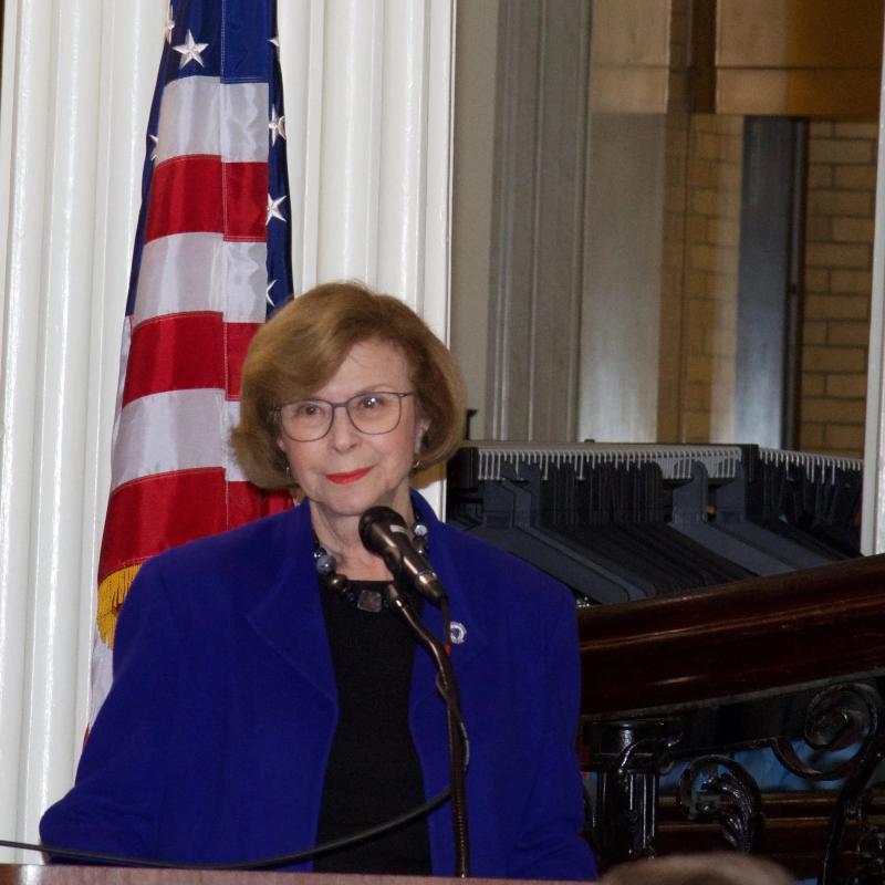 Woman stands at podium speaking.