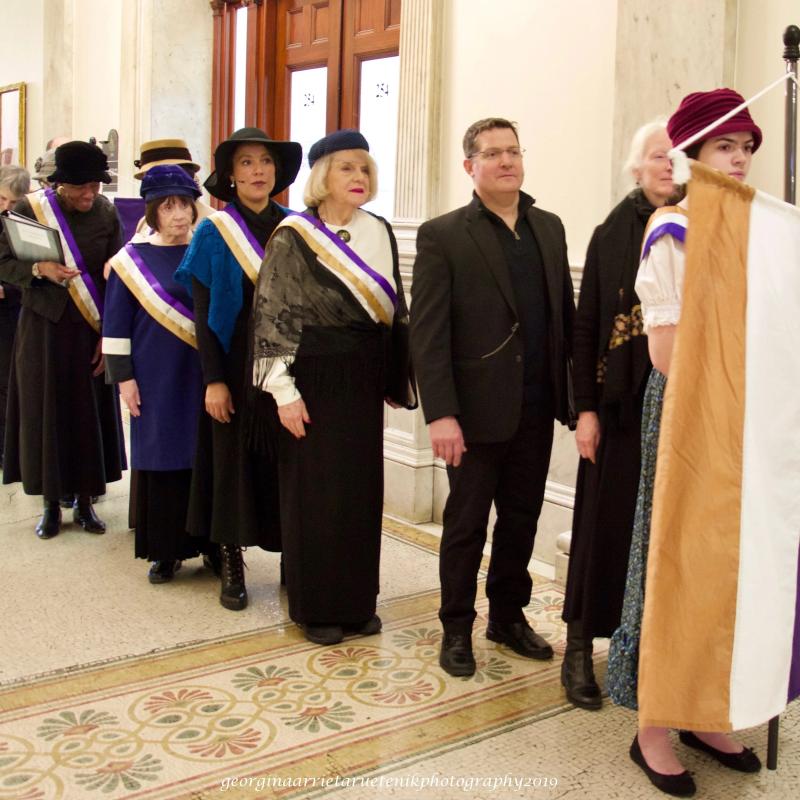 Eight people wearing sashes stand in line.