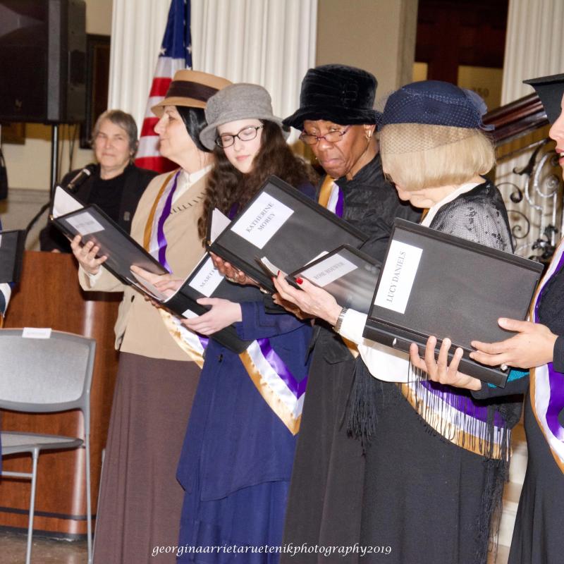 Group of women wearing sashes singing.