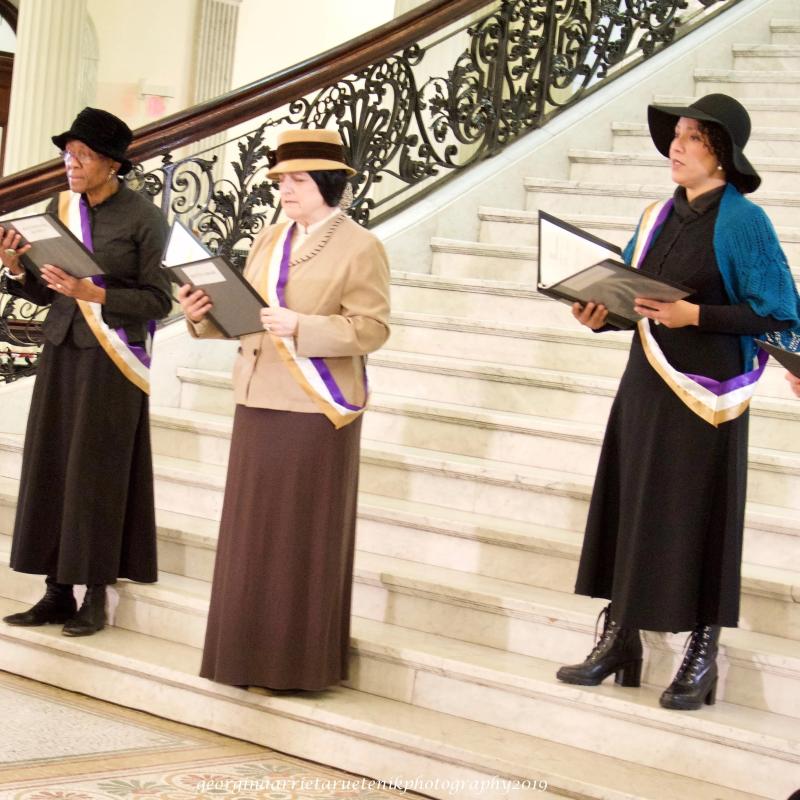 Women wearing sashes stand on steps.