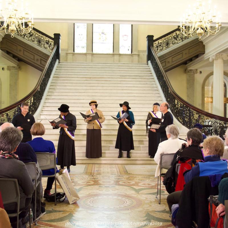 Women wearing sashes stand on steps.