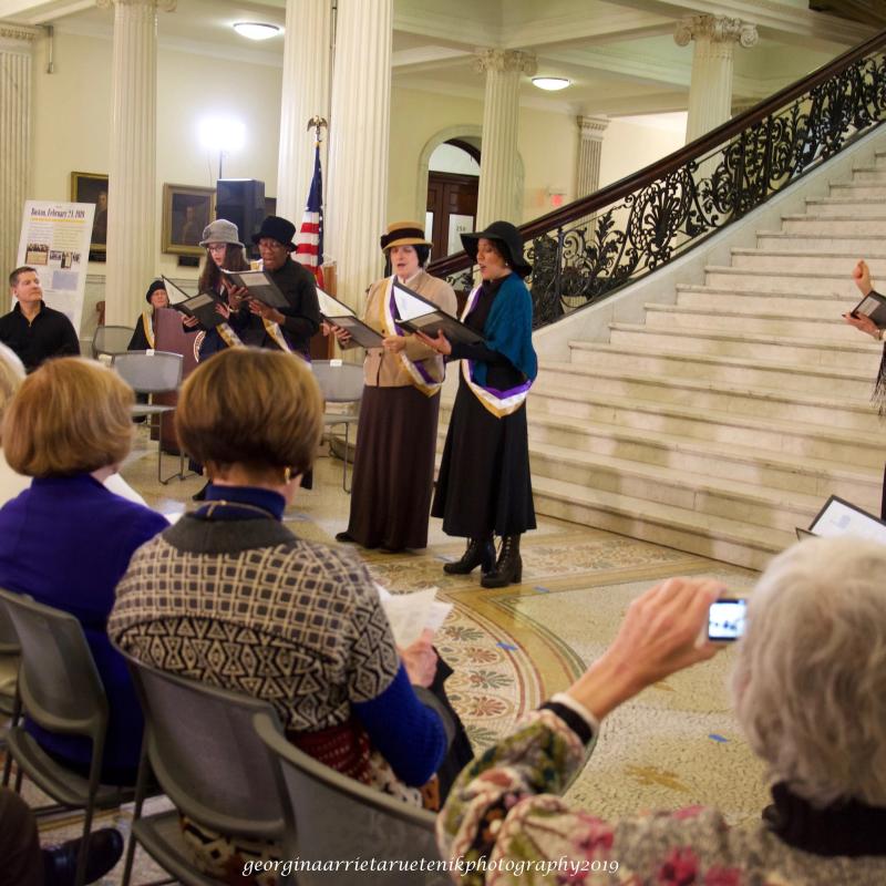 Women wearing sashes stand on steps.