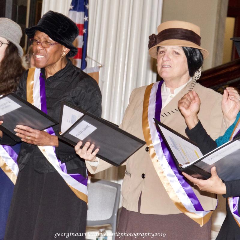 Women wearing sashes stand on steps.