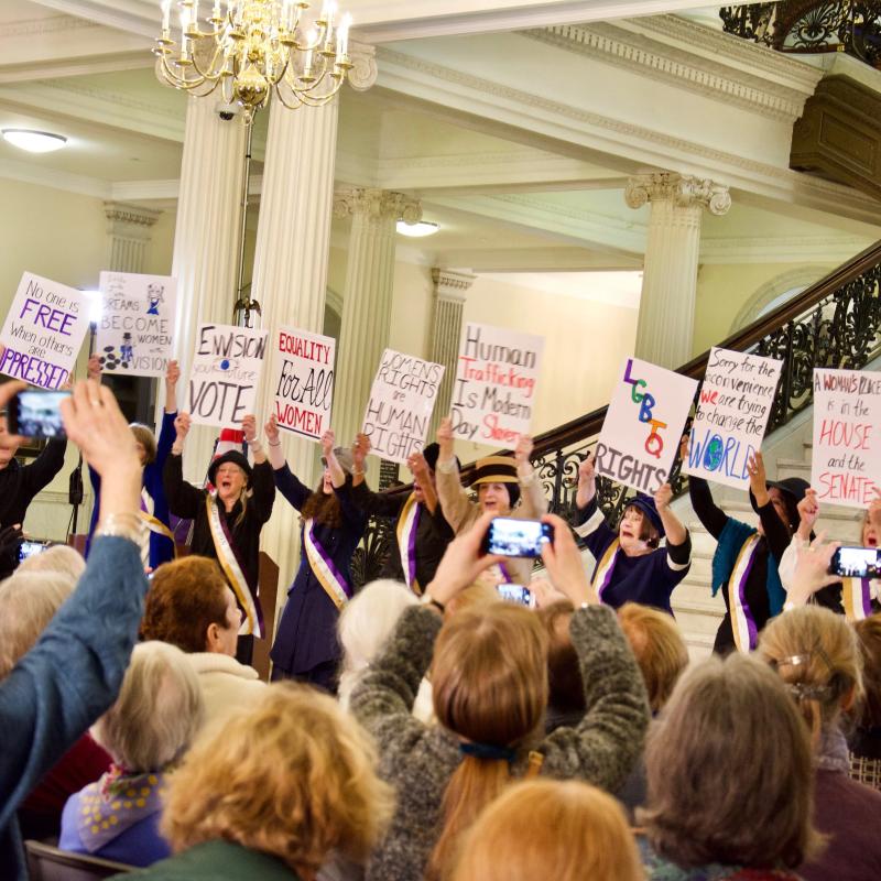 Crowd sits in chairs indoors.