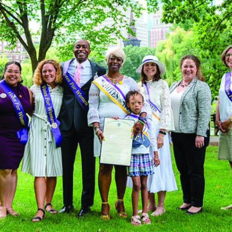 Seven adults and one child stand outside, wearing purple sashes.