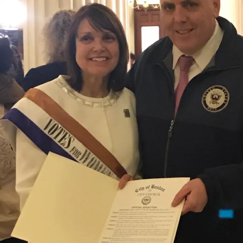 Two people smile at camera, holding papers.