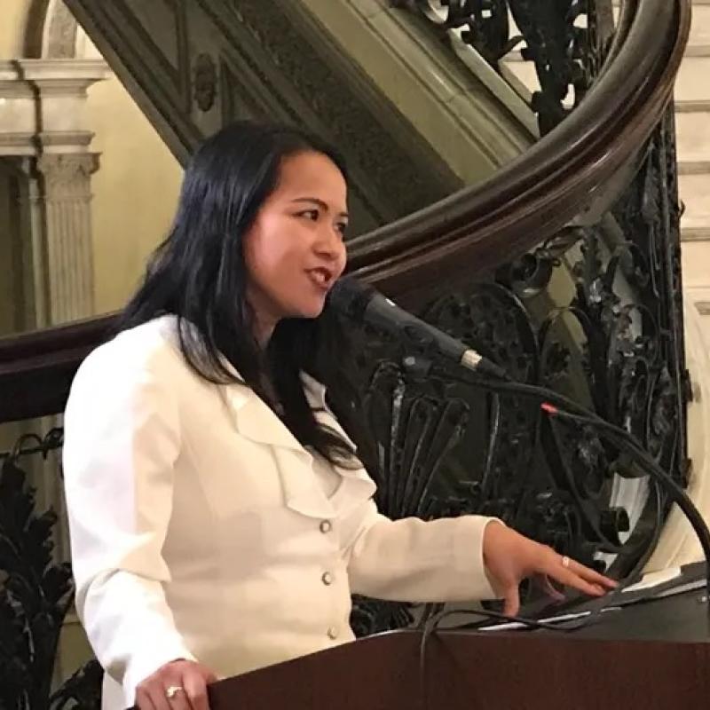 Woman stands at podium speaking.