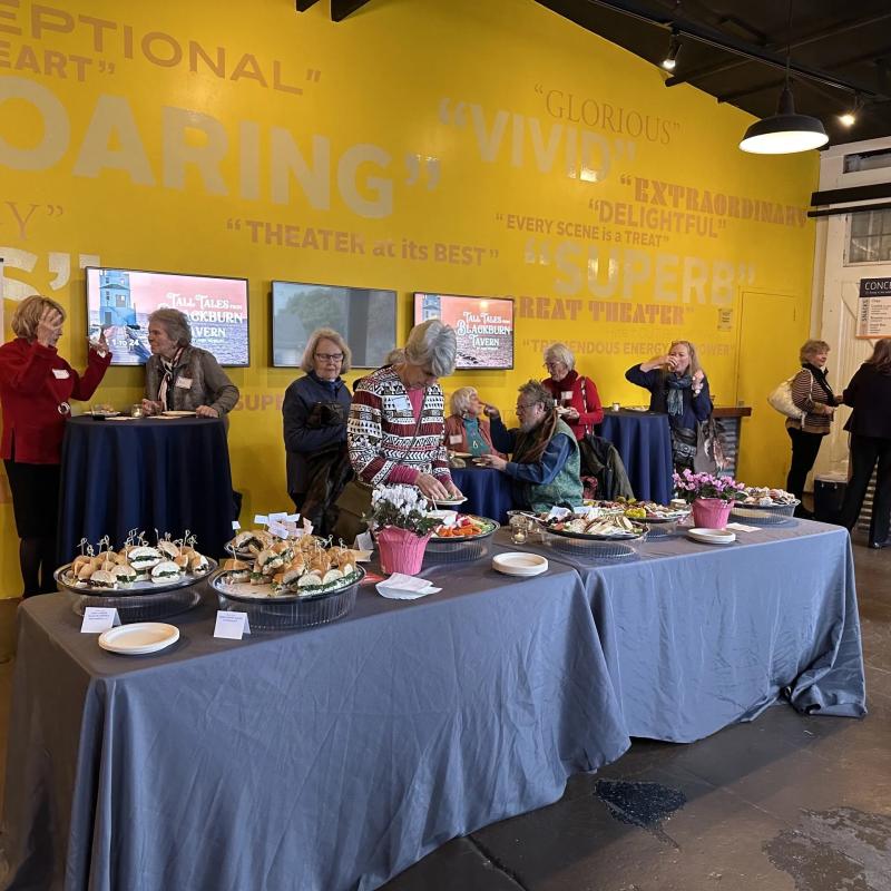 People standing by long table with food.