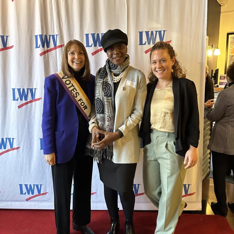 Three women stand indoors smiling.