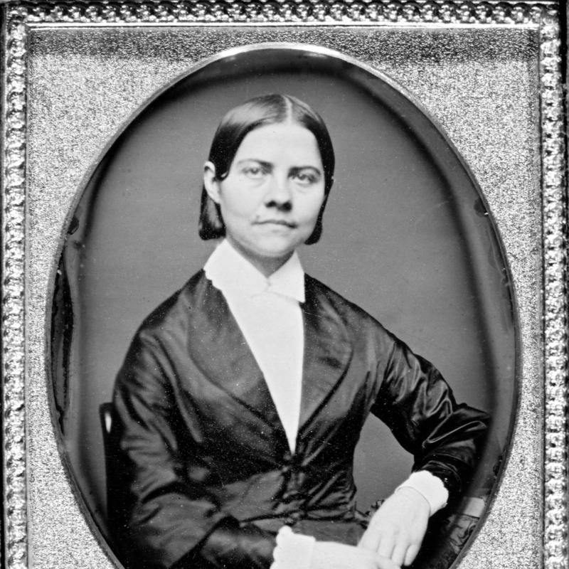 A portrait of a woman from the waist up wearing a black jacket and white blouse