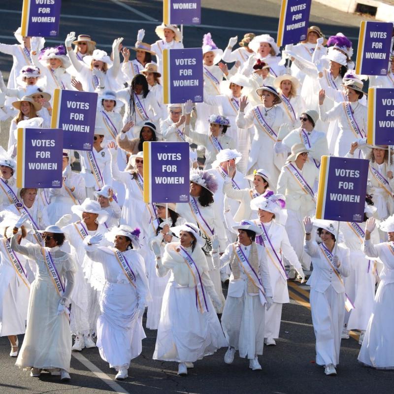 Women in white march in parade.