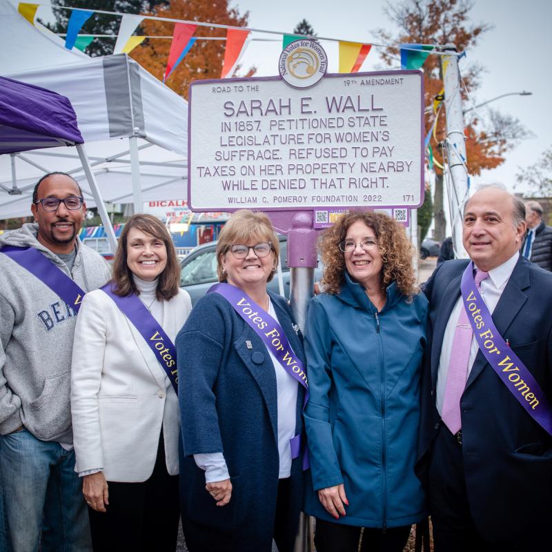 Five people stand in front of Sarah E. Wall suffrage marker.