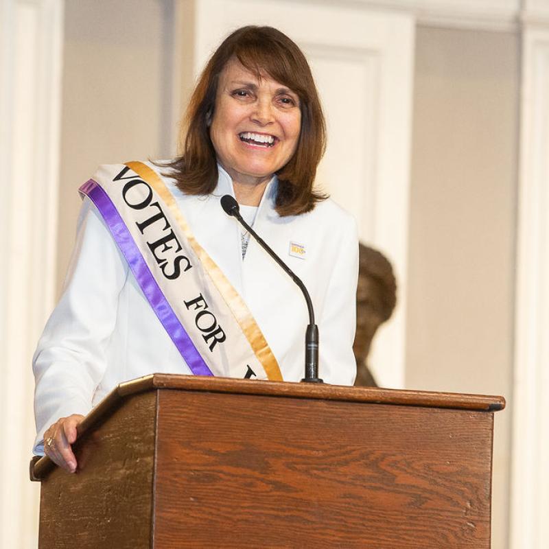 Woman stands at podium speaking.