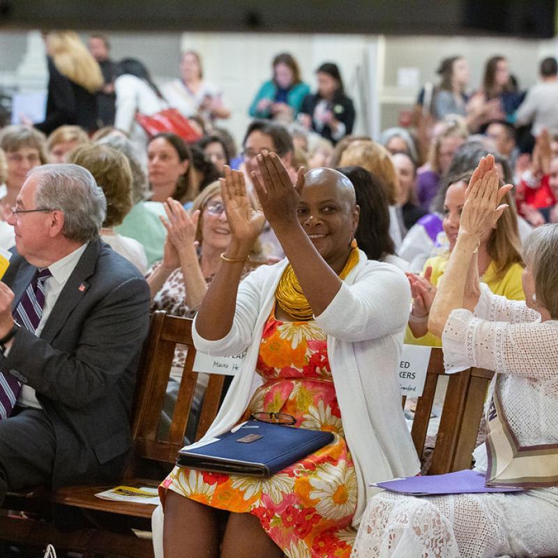 Crowd sits in chairs indoors.