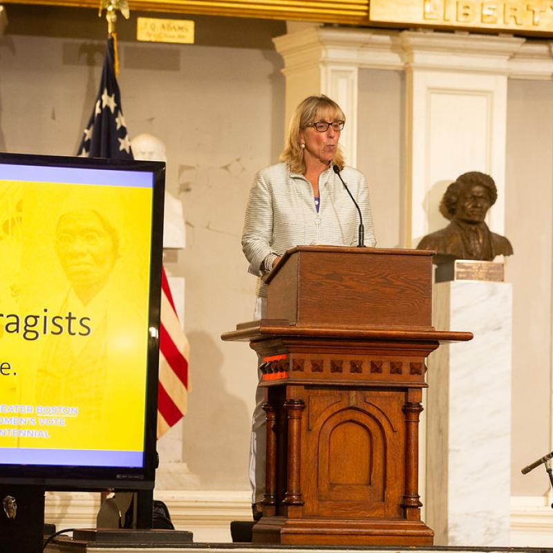 Woman stands at podium speaking.