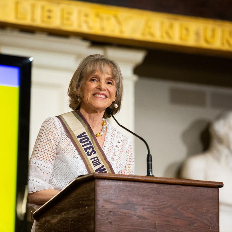 Woman stands at podium speaking.