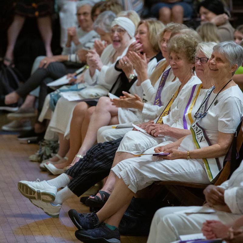 Crowd sits in chairs indoors.