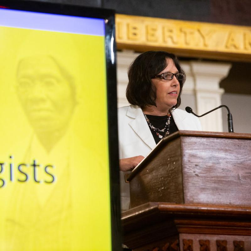 Woman stands at podium speaking.