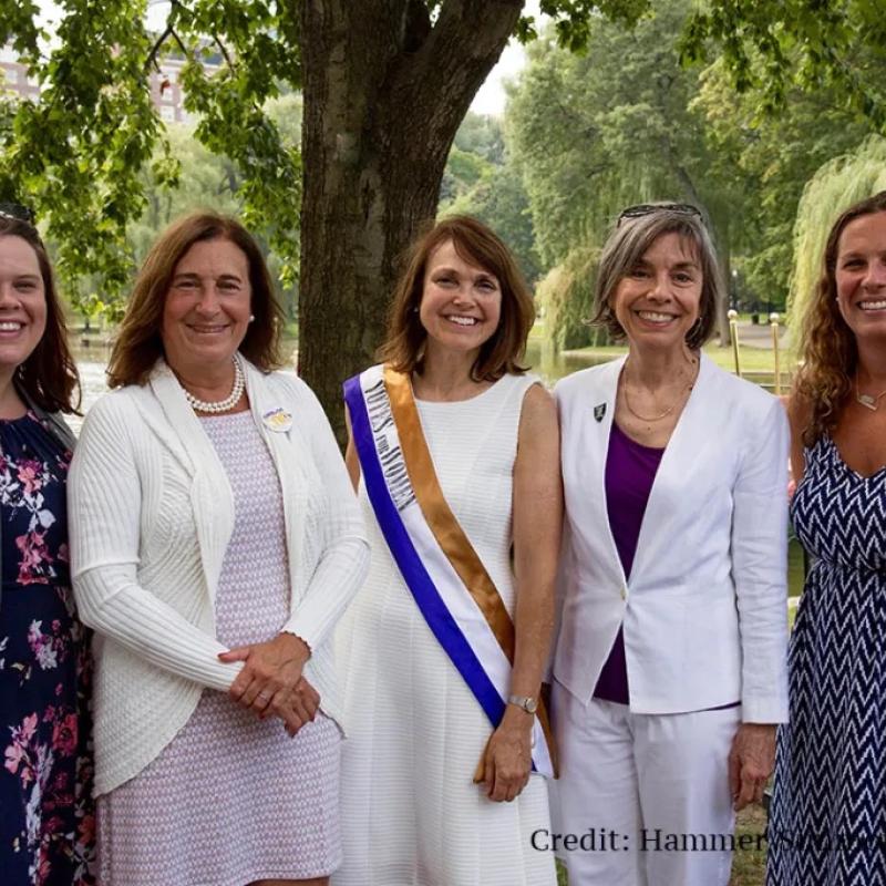Group of women stand together at a park, smiling.