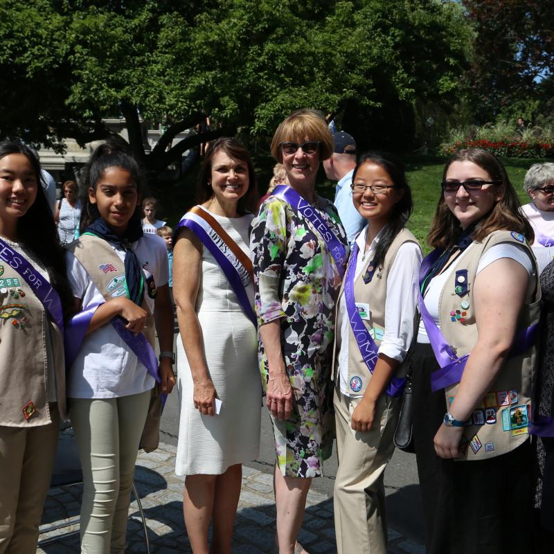 Group of women and teens wearing purple sashes and smiling.