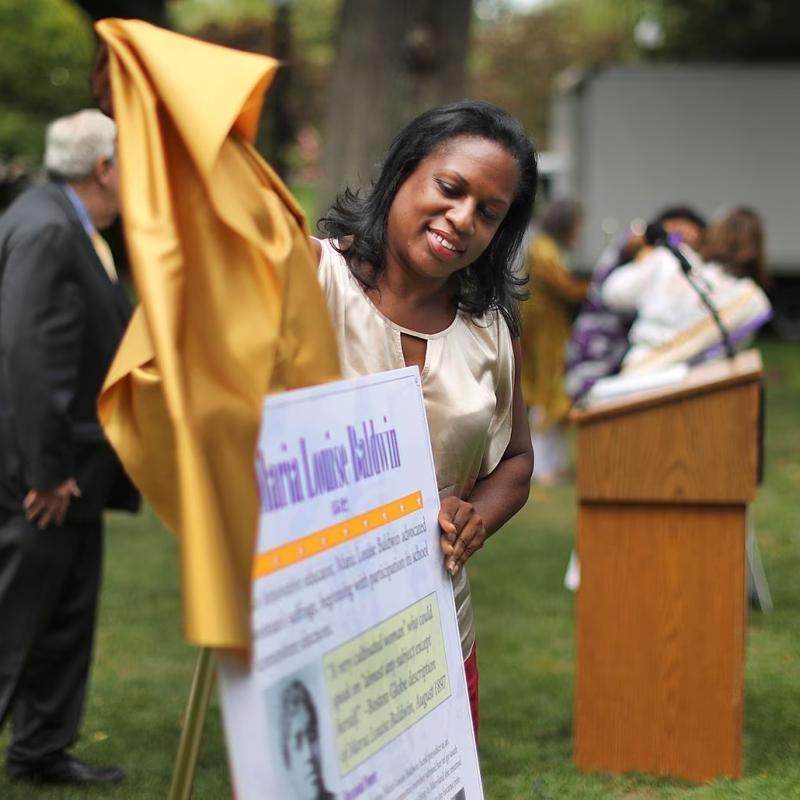 Woman pulls yellow cloth off of sign.