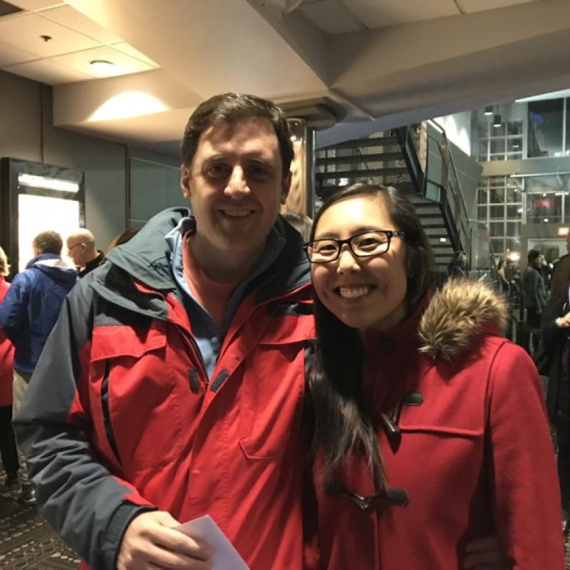 Man and woman stand indoors smiling.