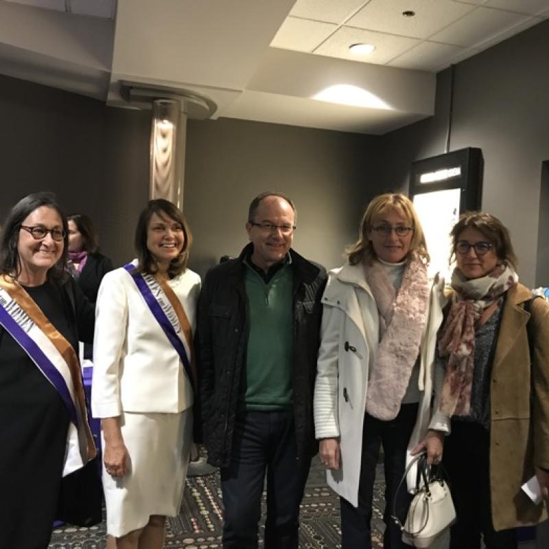 Five women stand indoors smiling.