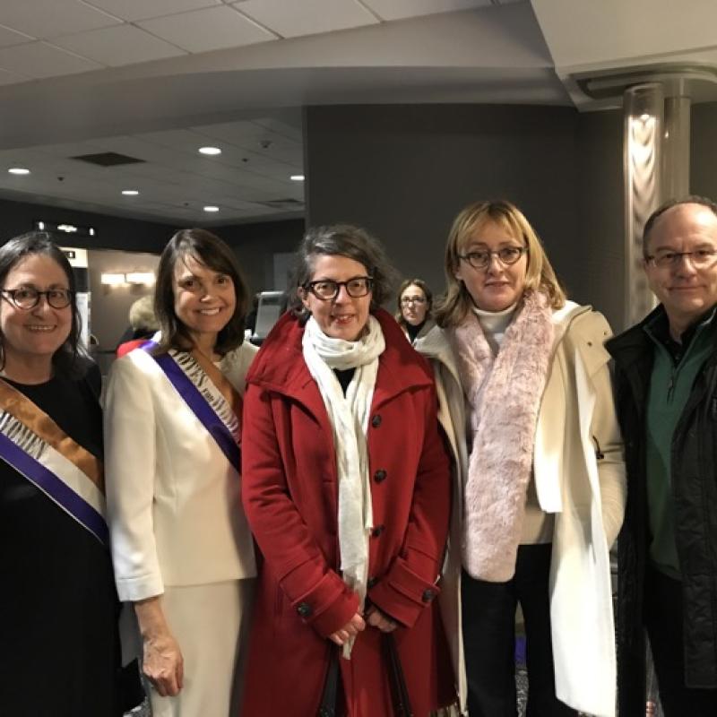 Four women and one man stand indoors smiling.