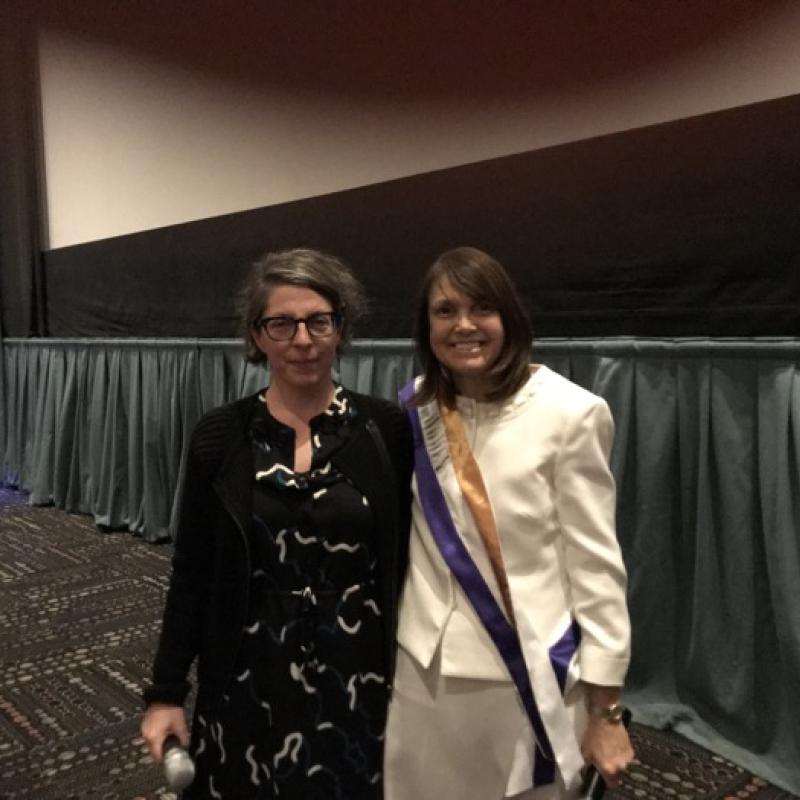 Two women stand smiling in movie theater.