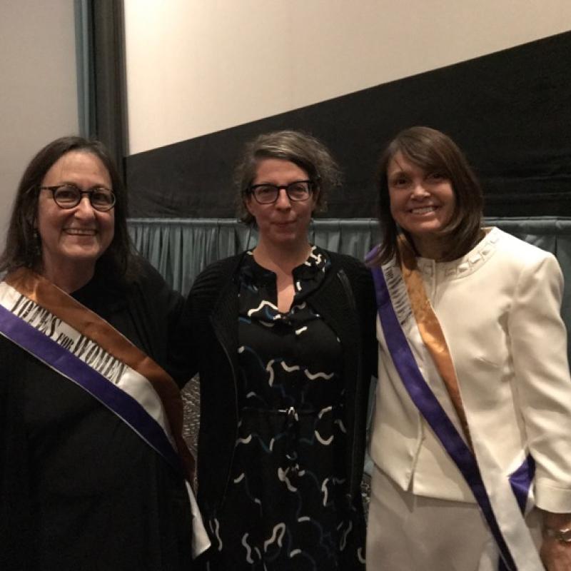 Three women stand indoors smiling.