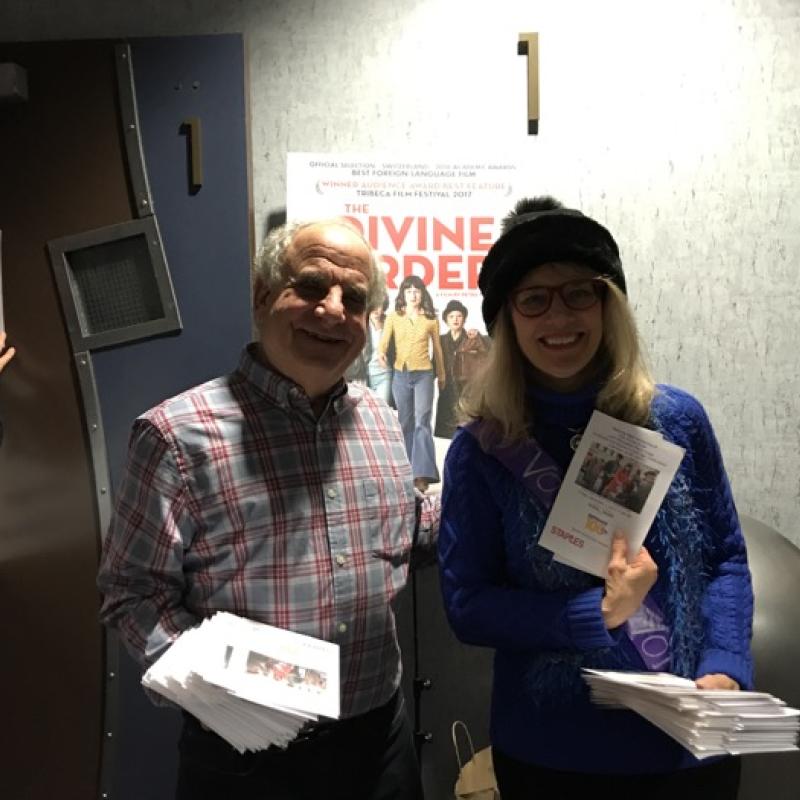 Two women stand indoors smiling.