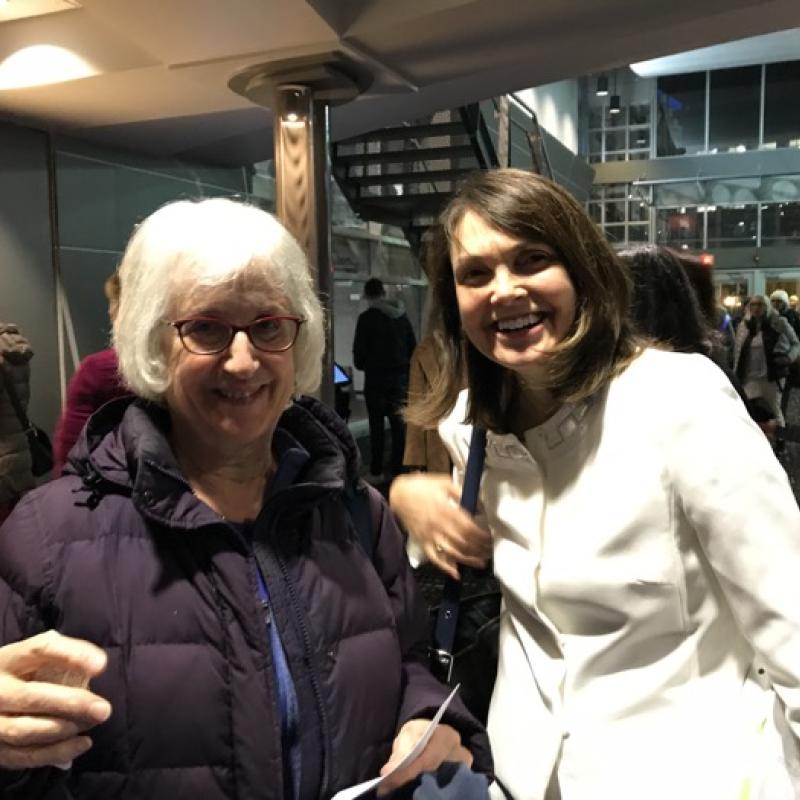 Two women stand indoors smiling.