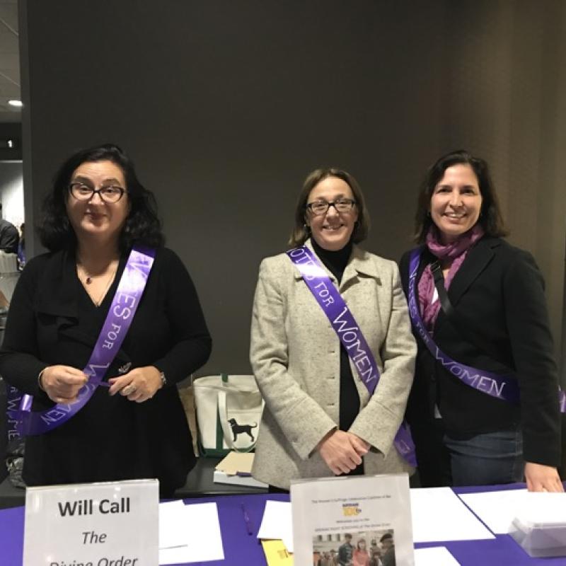 Three women stand indoors smiling.