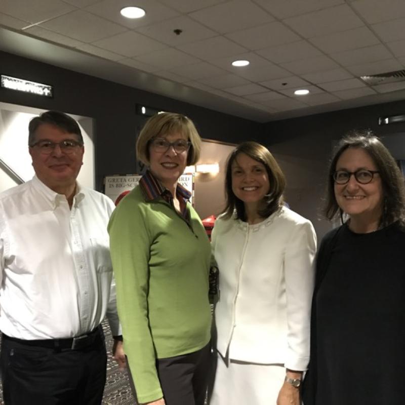 Four women stand indoors smiling.