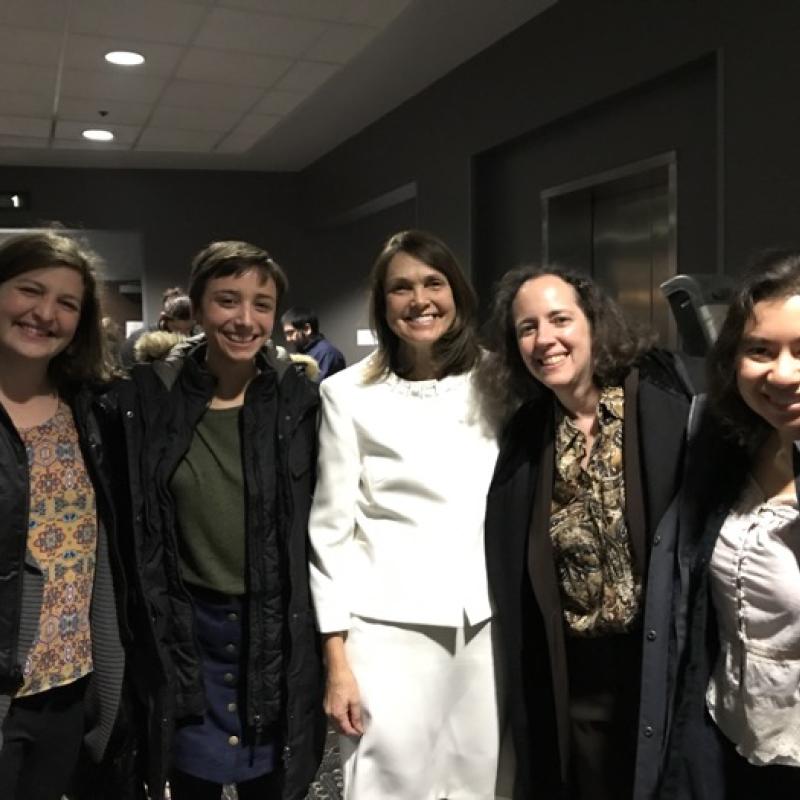 Five women stand indoors smiling.