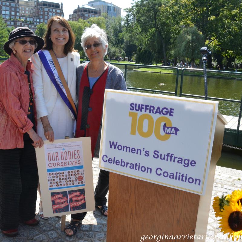 Three women stand next to pond.