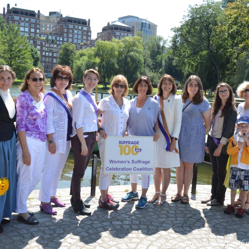 10 people stand outside next to Suffrage100MA sign.