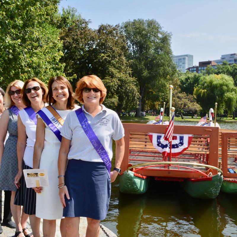 Six women stand outside wearing purple sashes.