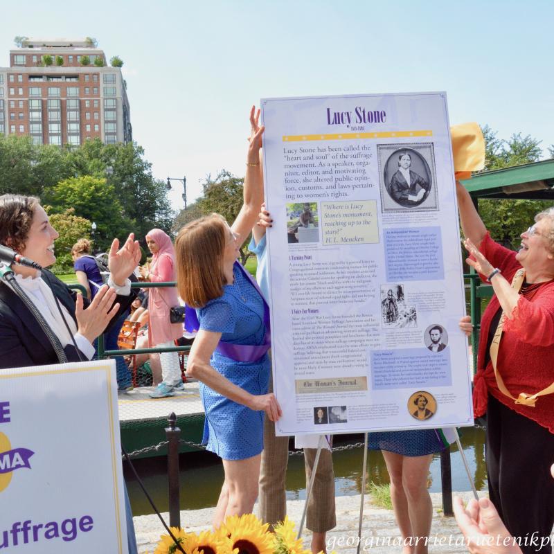 Two women with hands on tall white sign.